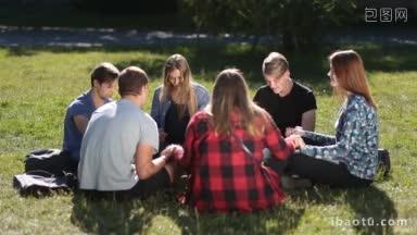 一群<strong>十几岁</strong>的大学基督徒朋友围坐在绿色的草地上祈祷，快乐的学生牵手冥想